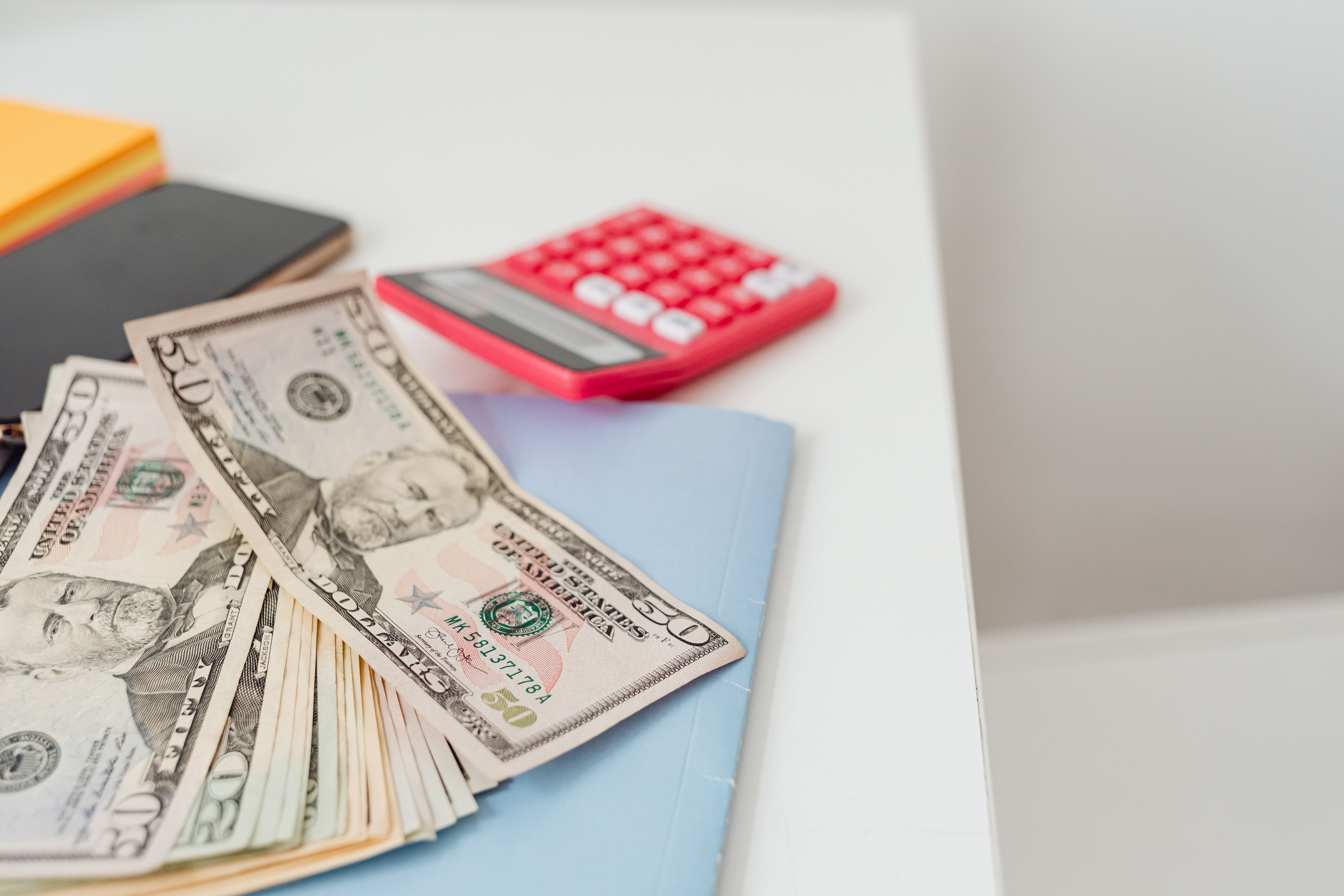 Billetes de dólar junto a una calculadora roja y cuadernos, representando la gestión del dinero