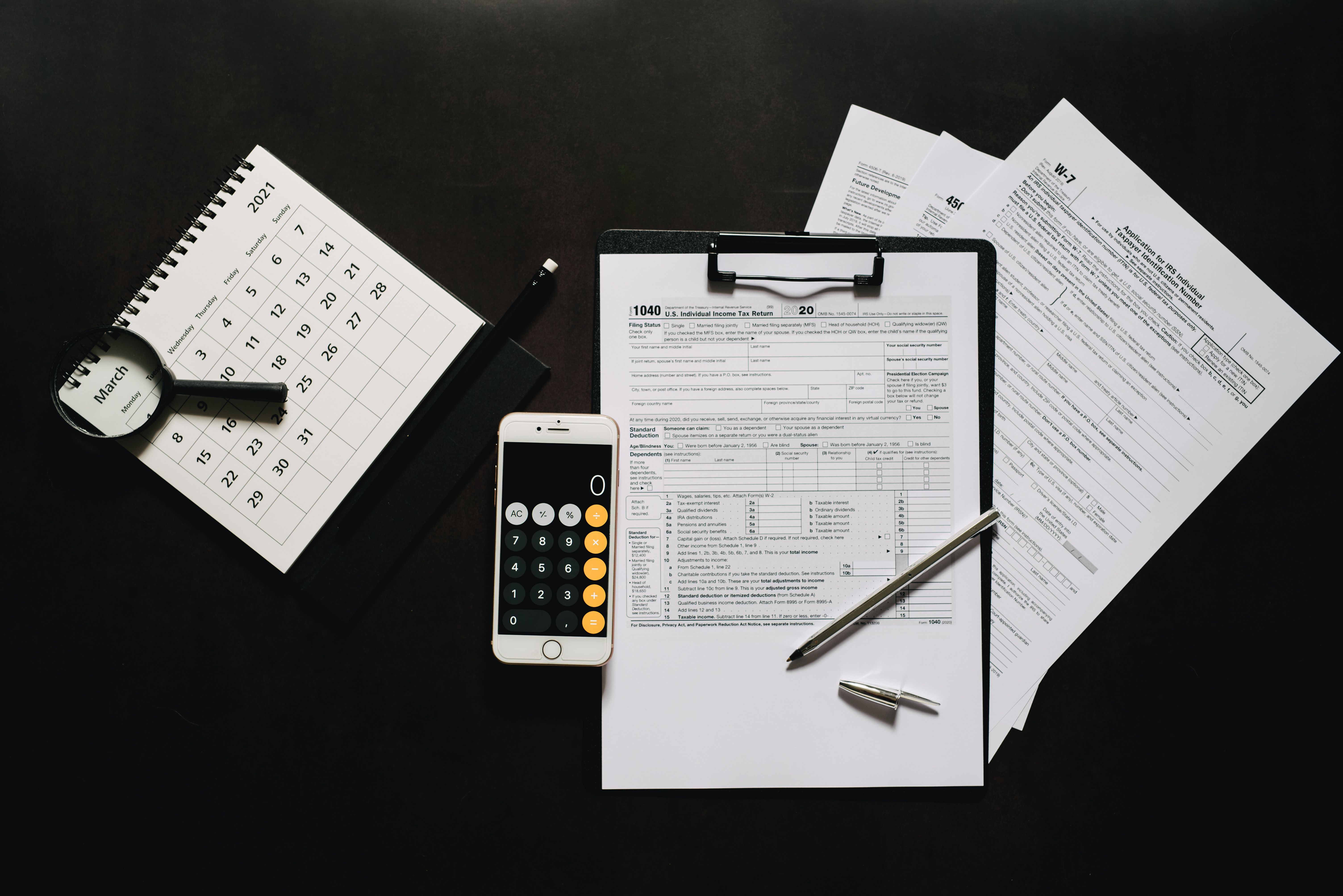 Formularios de impuestos, calendario, calculadora y lupa sobre un escritorio