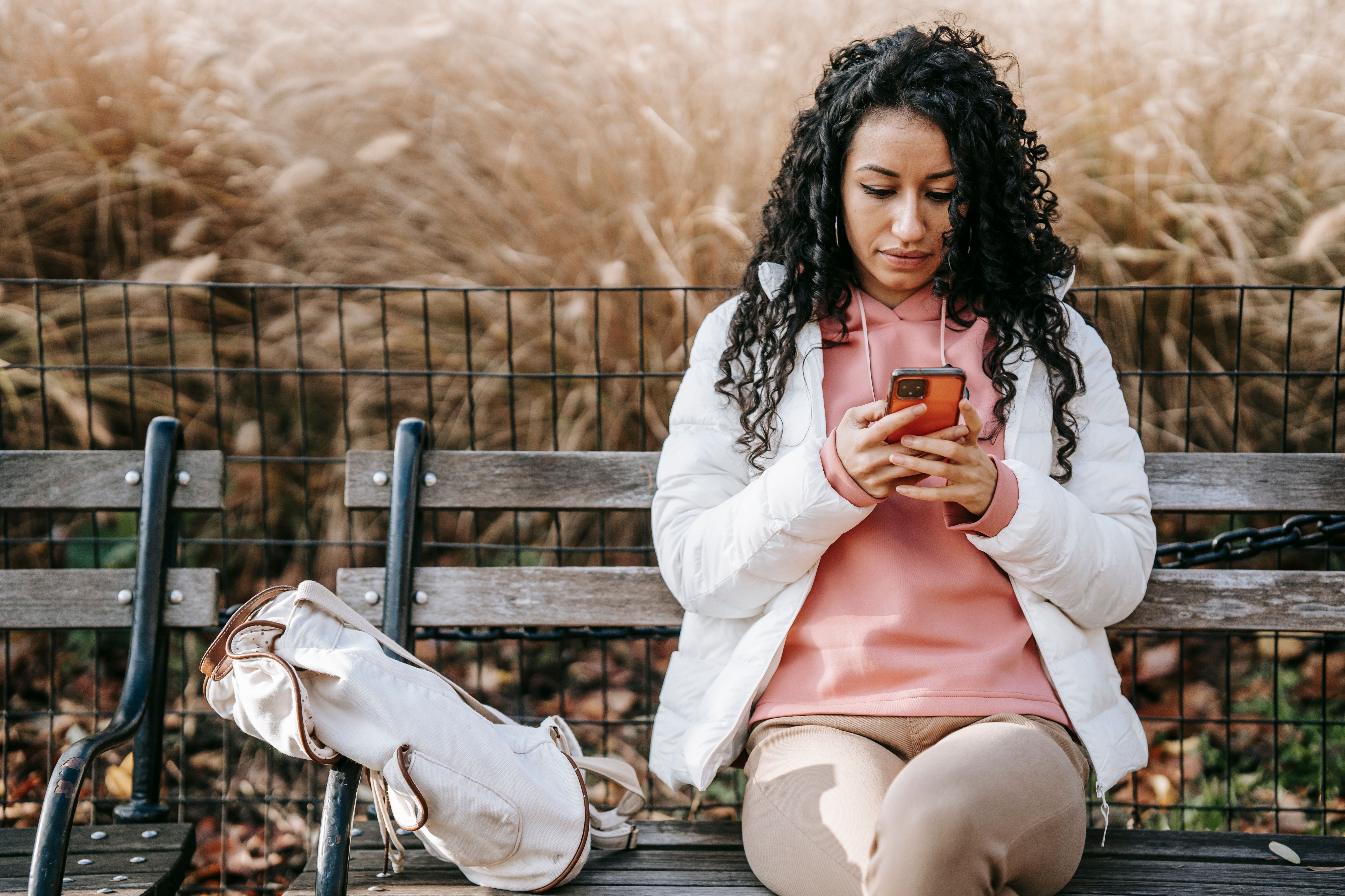 Mujer hispana con expresión seria escribiendo un mensaje de texto en su teléfono